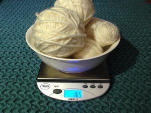 Cream colored mystery yarn balls in a bowl on a digital scale