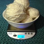 Cream colored mystery yarn balls in a bowl on a digital scale